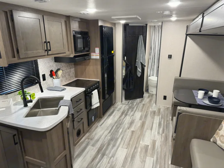 Spacious RV rental interior featuring a modern kitchen, dining area, and stylish wood-look floors.. Starcraft 26BHS 2024