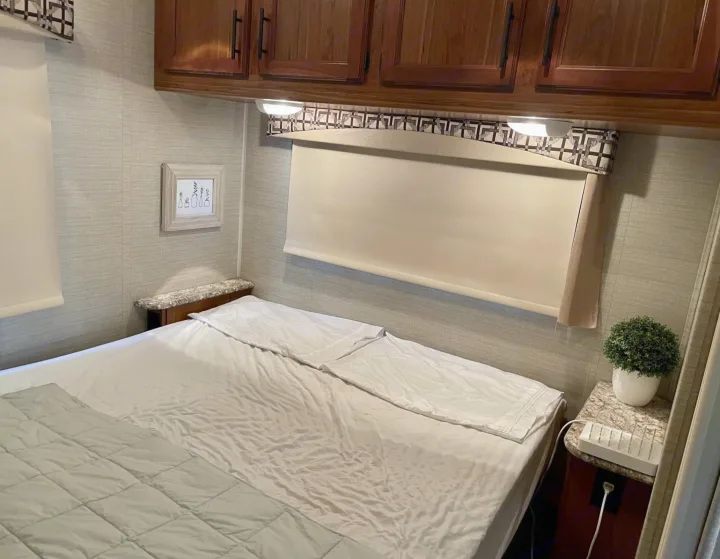 Cozy bedroom in an RV rental featuring a bed, window with blind, overhead cabinets, and small nightstands with decor and a charger.. Jayco Redhawk 2017