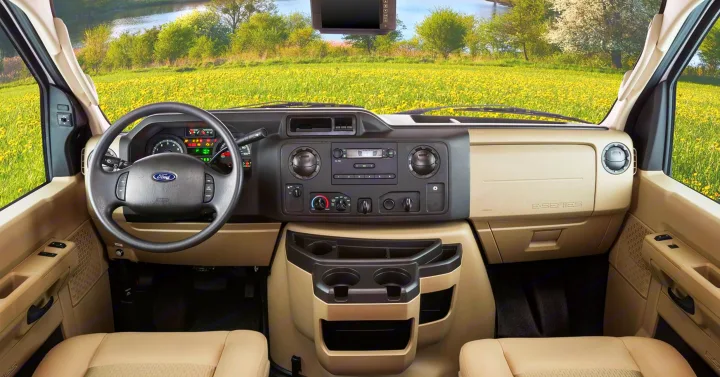 Inside a spacious RV rental: dashboard, steering wheel, and front cabin area with clear view of nature ahead.. Jayco Redhawk 2017