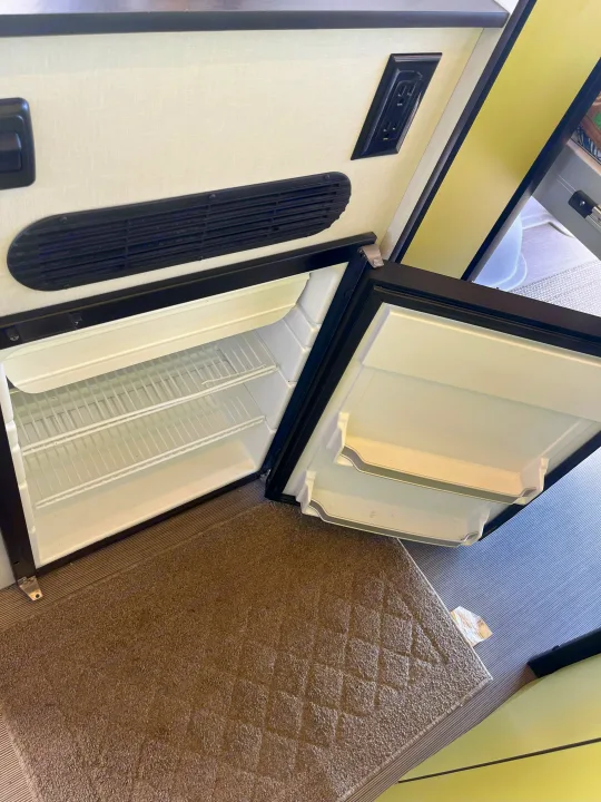Compact refrigerator/freezer combo open in an RV rental, revealing wire shelves and door storage. Outlets visible above.. Winnebago Revel 2019