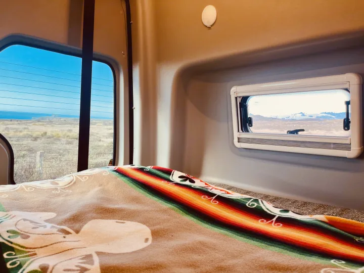 Relax in this RV rental's cozy interior, featuring a colorful blanket and distinct window views of coast and mountains.. Winnebago Revel 2019