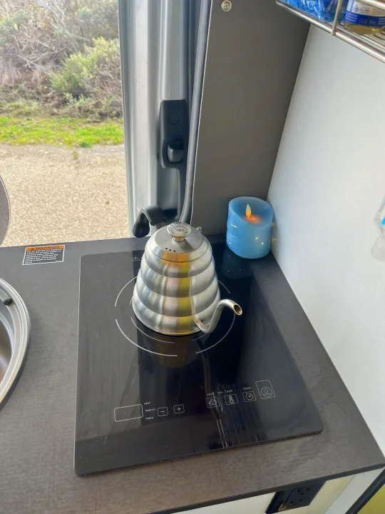 RV rental interior showing a gooseneck kettle with thermometer on an induction cooktop, beside a blue LED candle.. Winnebago Revel 2019