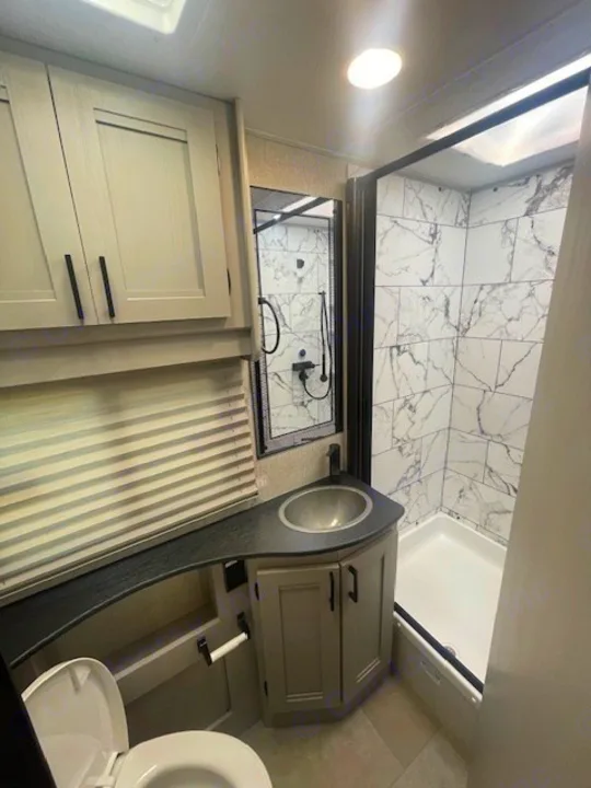 Modern RV rental bathroom featuring a sleek vanity, full shower with marble-look tiles, and a toilet. Ideal for travel.. Coachmen Freelander 2025