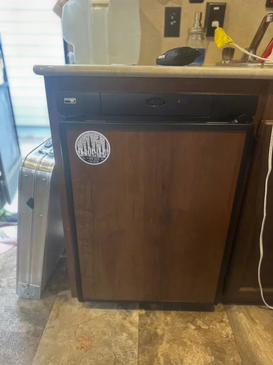 This RV rental's compact kitchen features a dark wood cabinet, small black refrigerator, countertop, and sink area.. Jayco Jay Flight SLX 2015