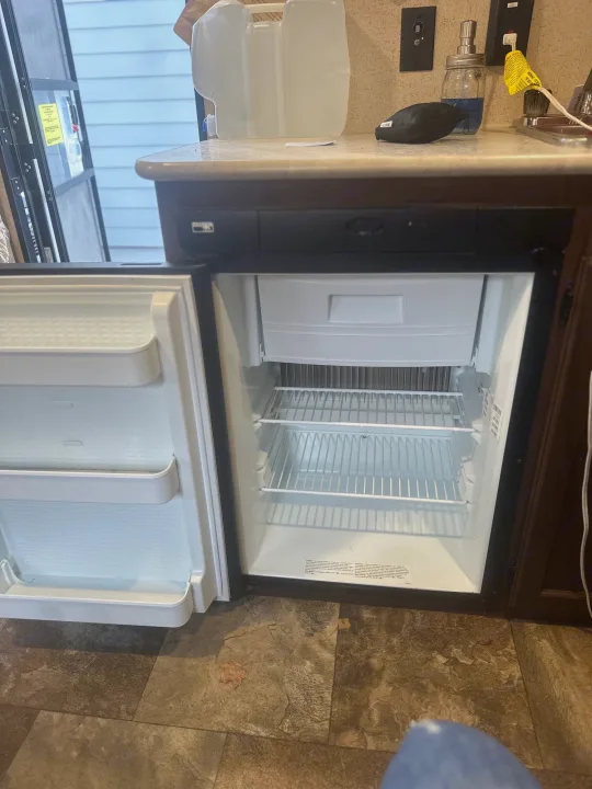 RV rental: An empty, open mini-fridge within a compact kitchen, showing interior shelves. Counter and water jug visible.. Jayco Jay Flight SLX 2015
