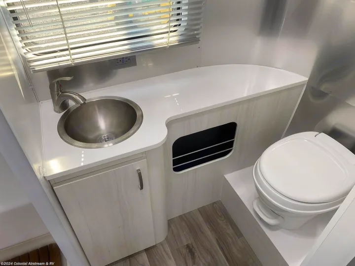 Modern RV rental bathroom: compact design with stainless sink, faucet, and white toilet. Light wood cabinetry & aluminum walls.. Airstream Sport 2019