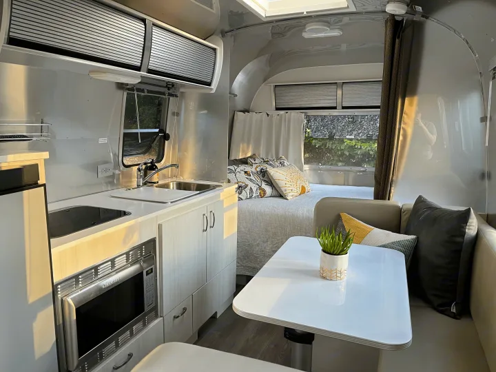 Interior of a modern Airstream RV rental. Shows a bright kitchen, cozy bed with patterned pillows, and seating area.. Airstream Sport 2019