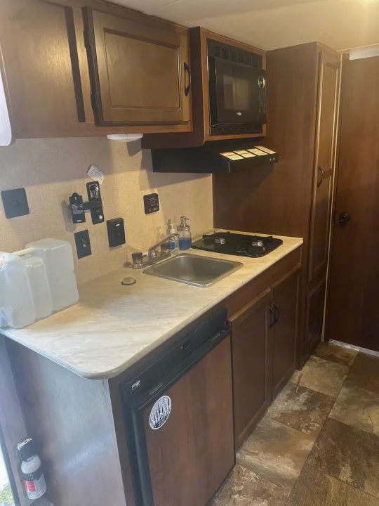 Compact RV rental kitchen with microwave, stove, sink, and fridge. Perfect for road trips and camping adventures!. Jayco Jay Flight SLX 2015
