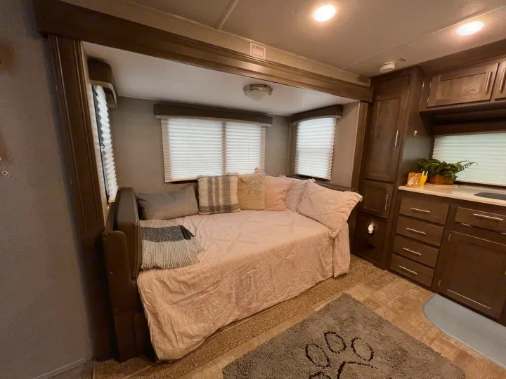 Cozy RV rental interior: a daybed with pillows, windows with blinds, dark wood cabinets, a counter, and a paw print rug.. Forest River Rockwood Mini Lite 2021