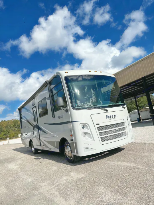 This sleek Pursuit motorhome, ideal for an RV rental, is parked outside on a sunny day under a blue sky with white clouds.. Forest River Coachmen Pursuit 2020