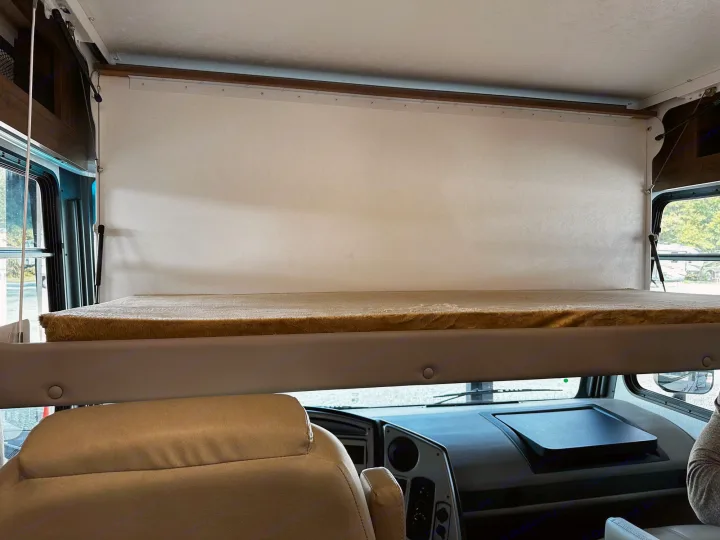 Inside an RV rental: an overhead bunk bed with a privacy curtain overlooks the cockpit. Perfect for travel and extra sleeping.. Forest River Coachmen Pursuit 2020