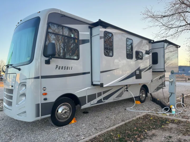 A spacious grey rv rental motorhome with extended slide-outs, fully hooked up at a gravel campsite, ready for adventure.. Forest River Coachmen Pursuit 2020