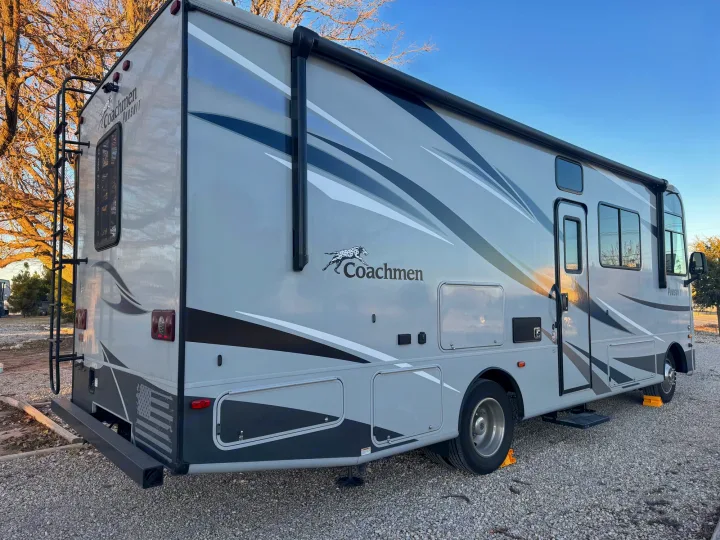 Gray Coachmen Pursuit RV rental parked on gravel. This motorhome offers travel freedom, featuring an awning & rear ladder.. Forest River Coachmen Pursuit 2020