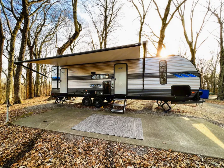 A serene RV rental campsite setup: travel trailer with extended awning, outdoor rug on concrete, surrounded by autumn leaves.. Forest River Salem 2022
