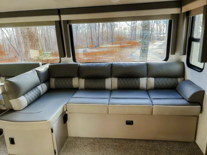 Spacious RV rental interior featuring an L-shaped couch, large windows, and a view of an autumn campsite.. Forest River Salem 2022