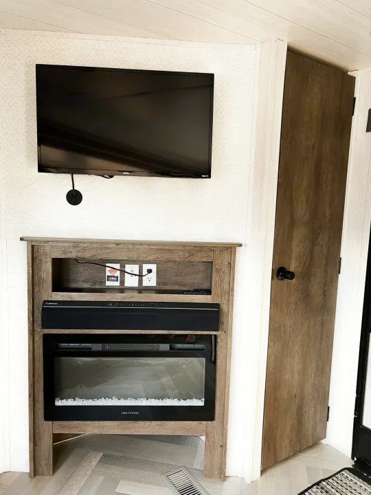 Modern RV rental interior features a wall-mounted TV, media console with electric fireplace and soundbar, plus a wooden door.. Forest River Salem 2022