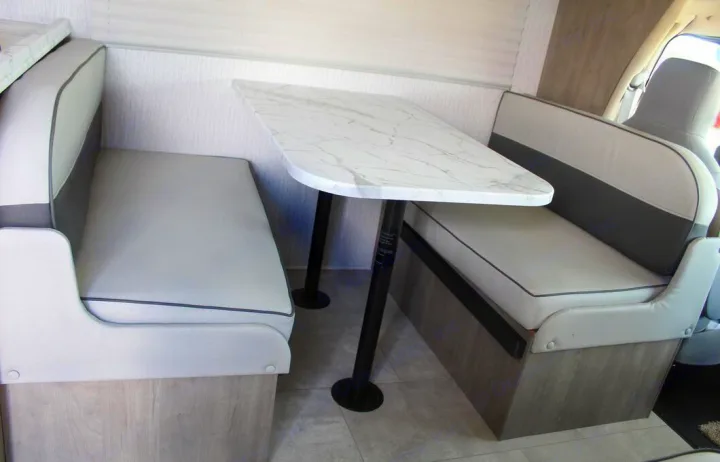 Comfortable RV rental dinette featuring stylish grey upholstered benches and a sleek marble-patterned table.. Freelander Coachman 2023
