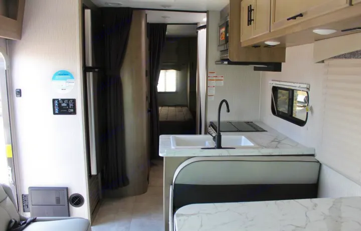 RV rental travel trailer interior: kitchen, dinette, and rear bedroom. Fridge and control panel near entrance.. Freelander Coachman 2023