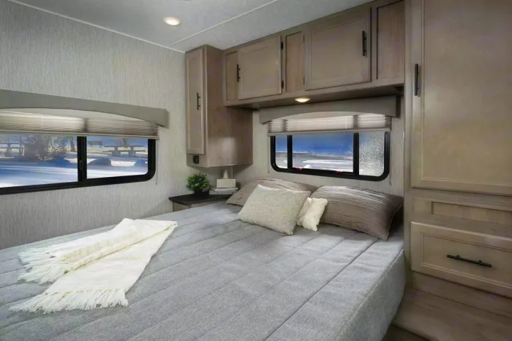 Cozy RV rental bedroom offers comfort with a large bed, ample storage, and scenic winter window views.. Freelander Coachman 2023