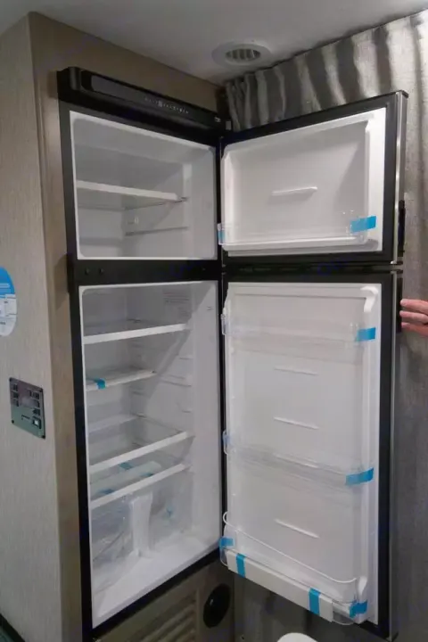 Spacious RV rental fridge with open doors, showing empty shelves & blue protective tape, ready for your trip.. Freelander Coachman 2023