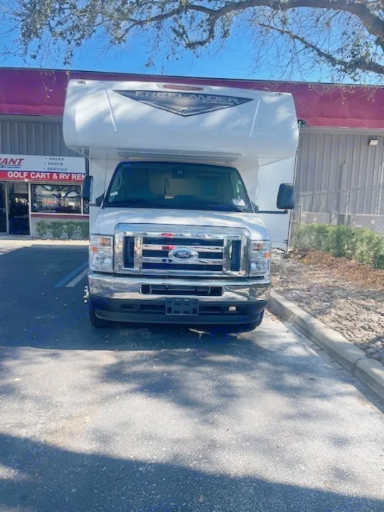 A white Ford Coachmen Freelander RV motorhome is parked outside an rv rental business, ready for adventure.. Coachmen FREELANDER 2025