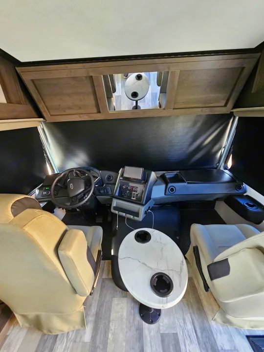 RV rental interior: A spacious cab with driver & passenger seats, a detailed dashboard, and a small table with cup holders. Blackout shades are visible.. FR3 FR3 Motorhome 2023