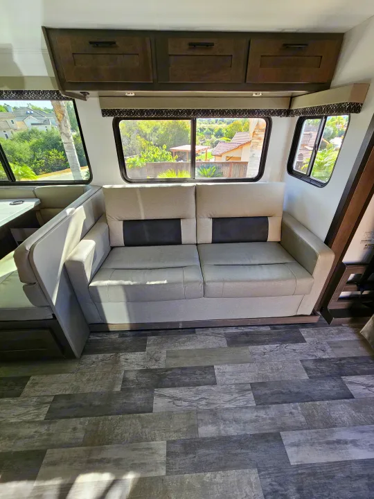 RV rental interior featuring a gray two-seater sofa, wood-look flooring, and windows with an outdoor view.. FR3 FR3 Motorhome 2023
