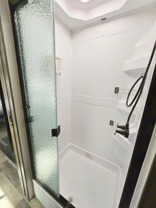 Inside a clean, compact RV rental shower with a textured glass door, white walls, and handheld showerhead.. FR3 FR3 Motorhome 2023