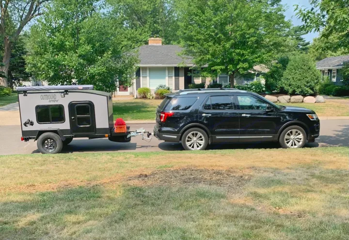 A black SUV tows a gray 'Outbound Extreme' camper trailer, parked on a suburban street. Ideal for an RV rental getaway.. Outbound Extreme 2021