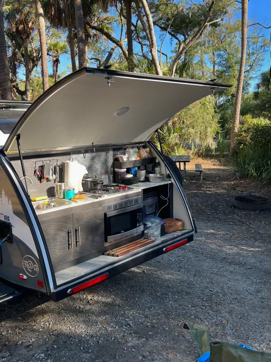 An rv rental teardrop trailer with a fully equipped outdoor kitchen, set in a sunny, treed campsite.. nuCamp T@G 2023