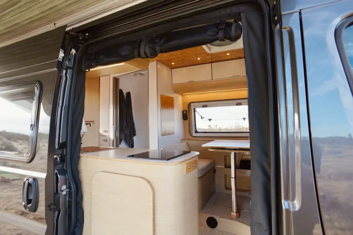 Step inside this modern campervan rv rental! View from the open door shows a spacious kitchen, dining area, and cozy interior.. Noovo Lite 2023