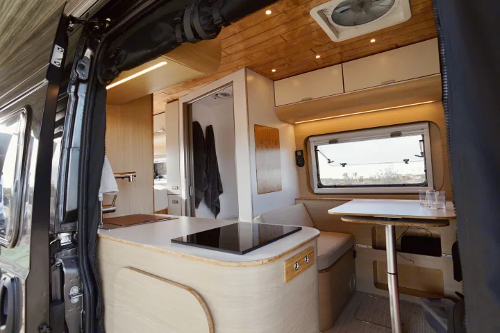 Step inside this chic rv rental: a bright camper van interior with a sleek kitchen, dining area, and a compact bathroom.. Noovo Lite 2023