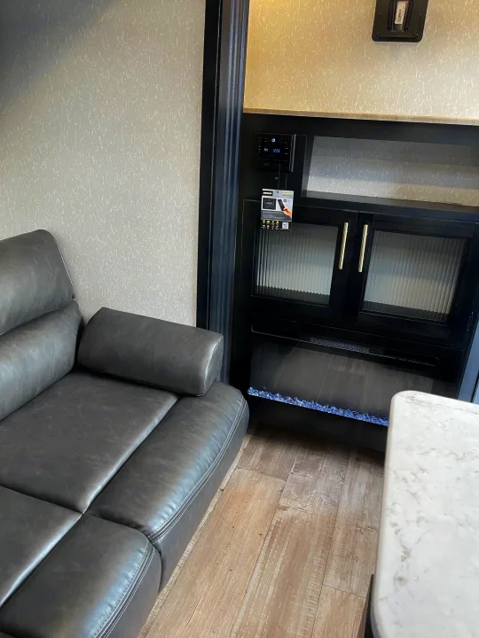An RV rental's cozy interior with a gray sofa, electric fireplace, wood-look floor, and built-in media system.. Forest River Patriot 26DBH 2022