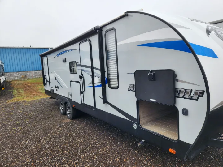 Grey and white travel trailer RV rental. Features blue accents, open storage, and a rolled-up awning.. Forest River Cherokee Alpha Wolf 2020