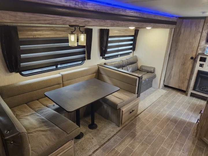 Comfortable rv rental interior featuring a dinette with booth seating, sofa, wood-look paneling, and ambient blue lighting.. Forest River Cherokee Alpha Wolf 2020