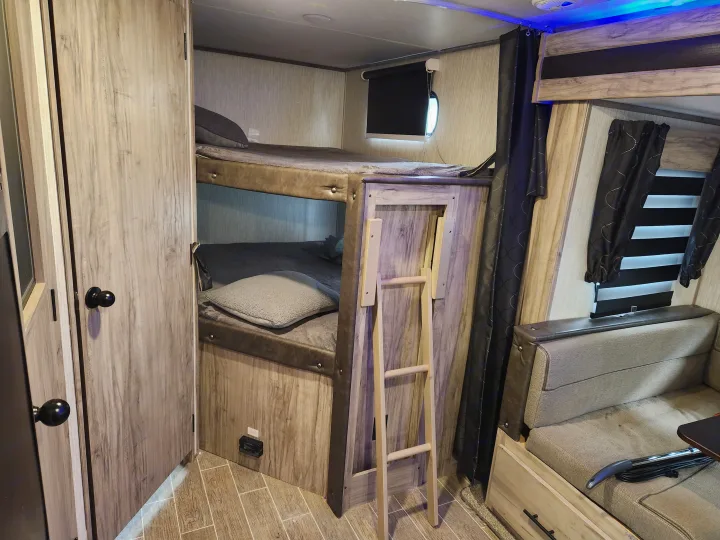 RV rental interior: bunk beds with ladder, compact sleeping/living space, modern wood-grain finishes and blue LED accents.. Forest River Cherokee Alpha Wolf 2020