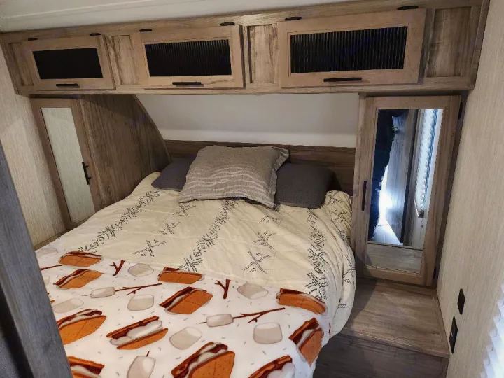 Cozy RV rental bedroom featuring overhead cabinets, mirrored wardrobes, and a bed with a fun s'mores blanket.. Forest River Cherokee Alpha Wolf 2020