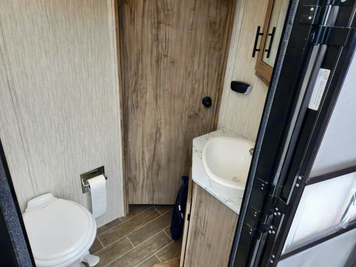 RV rental bathroom: Features a compact toilet, sink, and stylish wood-look interior. Perfect for your travels.. Forest River Cherokee Alpha Wolf 2020