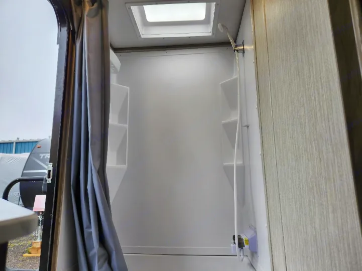 Inside an RV rental: a bright, compact shower with a skylight, handheld shower head, and built-in shelves.. Forest River Cherokee Alpha Wolf 2020