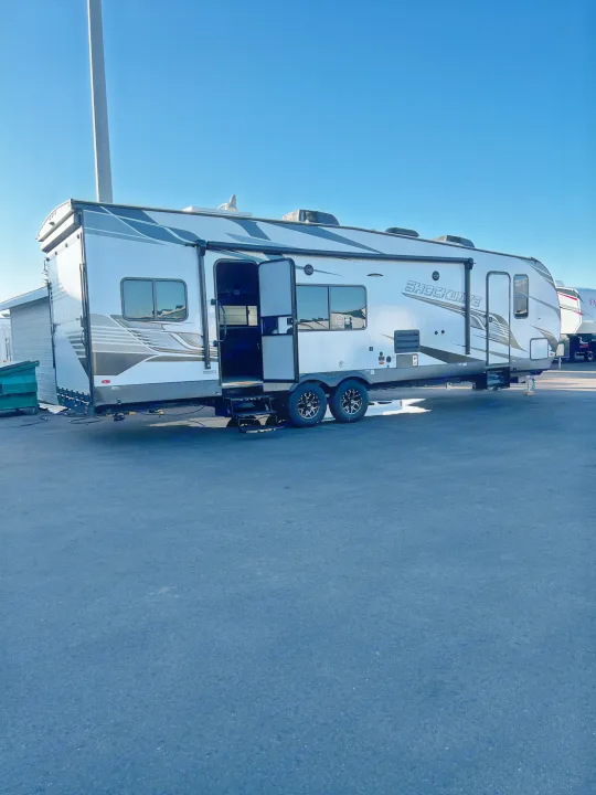 A white Shockwave RV rental with modern graphics and an open door sits on asphalt under a clear blue sky.. Forest River Shockwave 2023