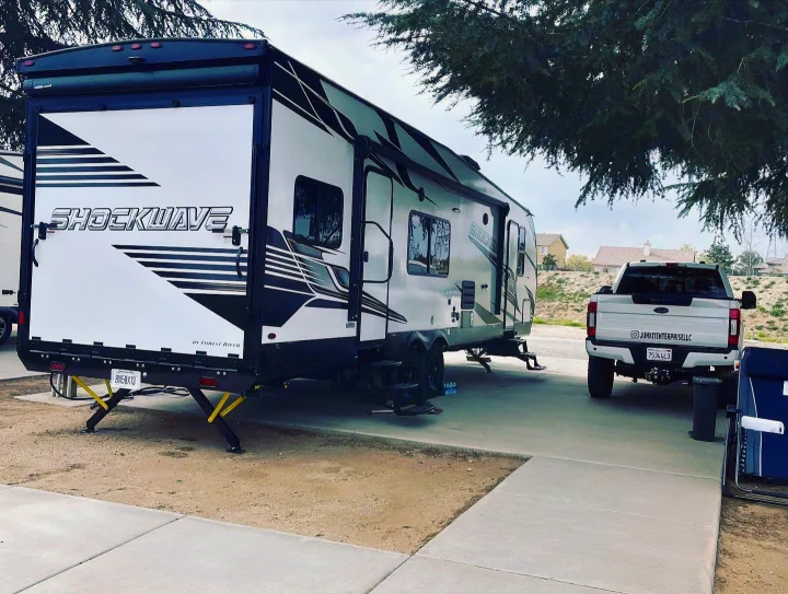 Explore camping & travel with this RV rental! A Forest River Shockwave toy hauler and pickup truck are parked at a recreation site.. Forest River Shockwave 2023