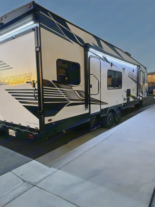 Illuminated white and black Shockwave toy hauler RV rental parked on concrete at night, ready for adventure.. Forest River Shockwave 2023