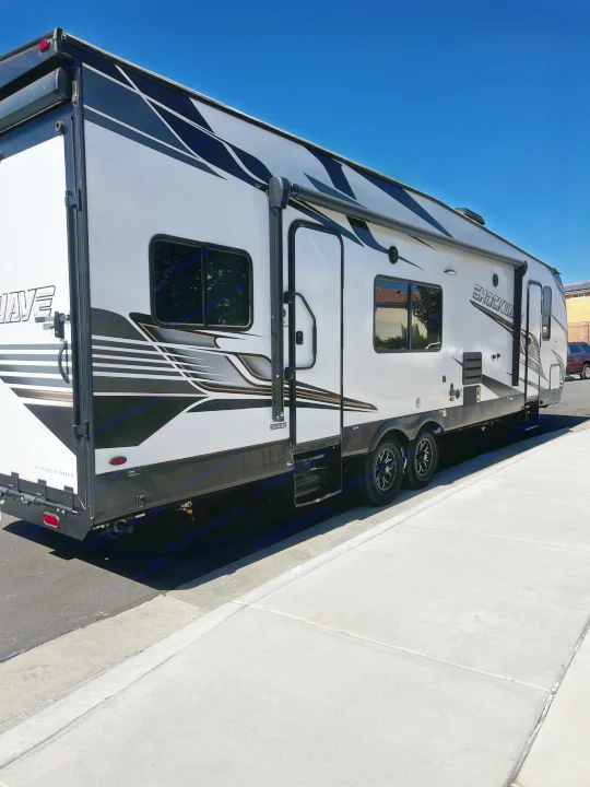 A large, modern white and black RV rental (travel trailer) is parked on a sunny street, ready for adventure.. Forest River Shockwave 2023