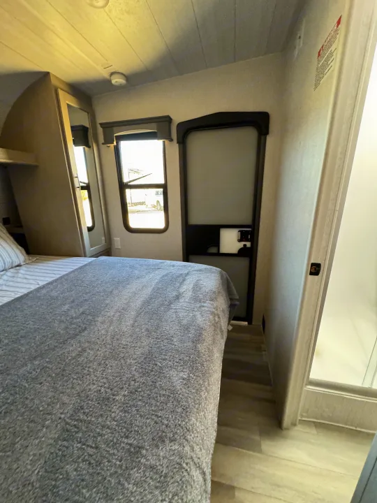 Compact RV rental bedroom featuring a cozy bed, window, and door, ideal for comfortable road trips.. Forest River Shockwave 2023