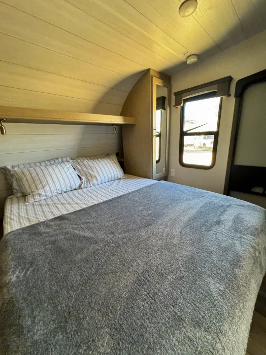 Experience comfort in this RV rental bedroom: cozy bed, storage, and natural light. Ideal for your next road trip.. Forest River Shockwave 2023