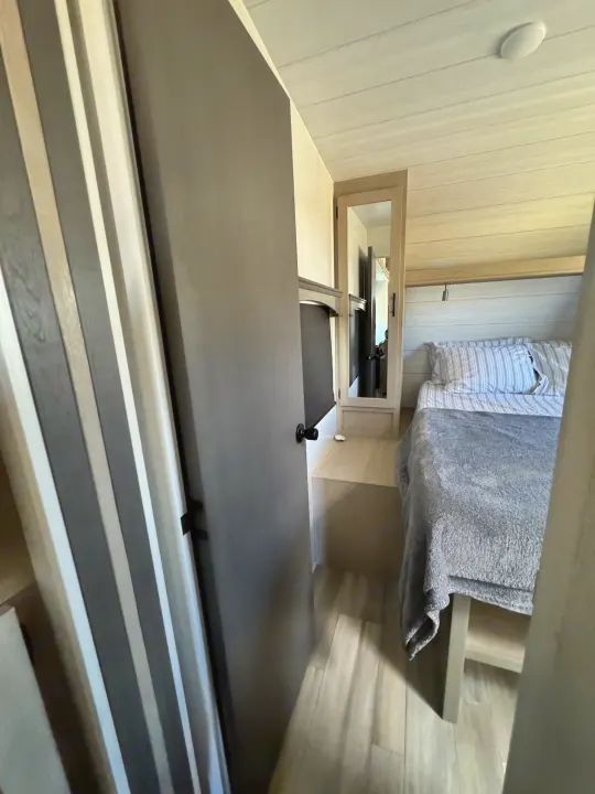 RV rental bedroom interior: a striped bed, mounted TV, and mirrored cabinet in a modern, compact space.. Forest River Shockwave 2023