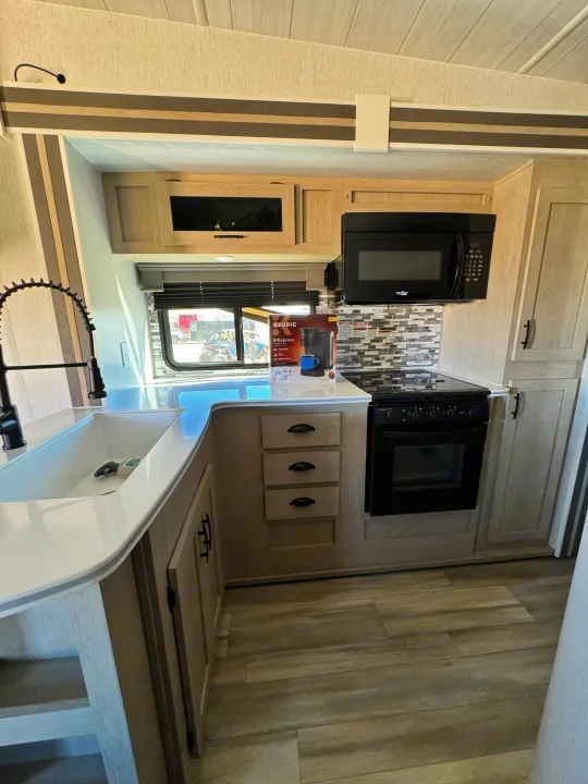 Well-equipped RV rental kitchen featuring light wood cabinets, a large sink with black faucet, microwave, and stove.. Forest River Shockwave 2023