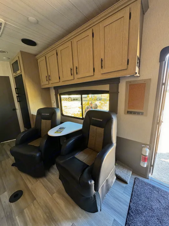 Spacious RV rental interior with two comfortable recliners, overhead cabinets, and a scenic window view, perfect for relaxation.. Forest River Shockwave 2023