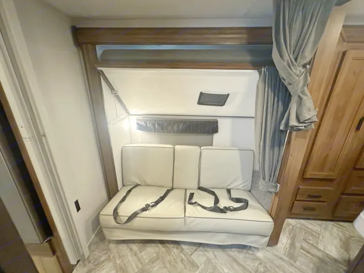 Compact RV rental interior with a light-colored convertible sofa, black seatbelts, wood cabinets, and an upper fold-down bunk.. Forest River Forester 2022