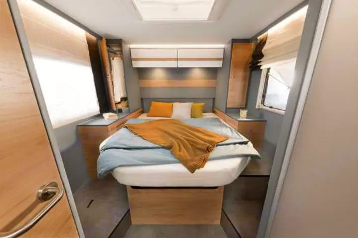 Modern RV rental bedroom with compact bed, wood accents, and integrated storage units.. Dethleffs Just T7052 DBM 2024